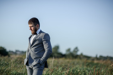 Handsome groom in grey suit poses on the green field