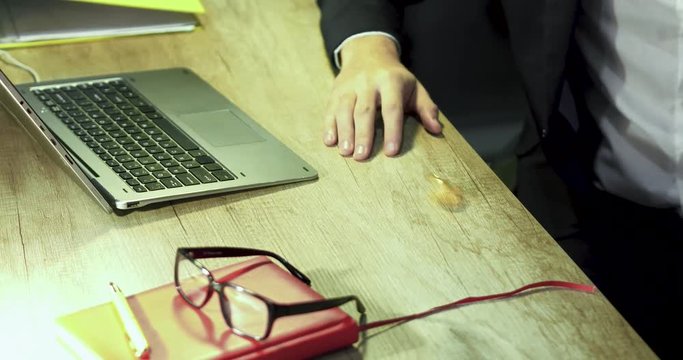 Laptop, red notebook, glassess and bitcoin lie on the table. A part of male suit is visible. Crypto currency concept.