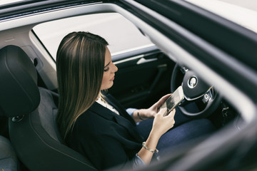 Young woman in her car driving looking smartphone and programming car with an app