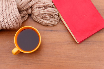 Cup of coffee, knitted scarf and book on wooden background