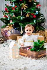 Obraz na płótnie Canvas A beautiful little baby is playing around a Christmas tree