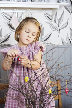 Little girl decorating twigs with Easter eggs