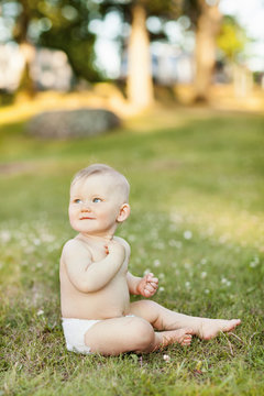 Baby wearing nothing but diaper sitting on grass and looking over shoulder
