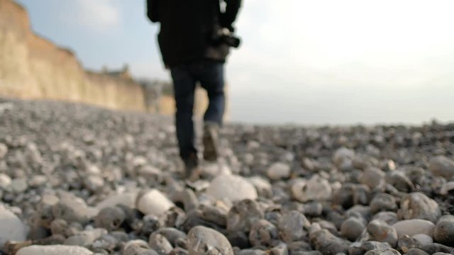 The back of the photographer walking on the rocks by the beach