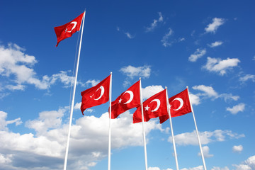 Turkish flags flutter in the wind against a blue sky.