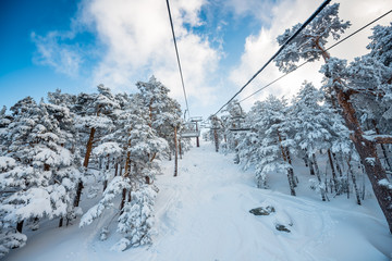 A winter view of a ski resort full of fresh snow taken from the chairlift going through a forest, in Madrid, Spain