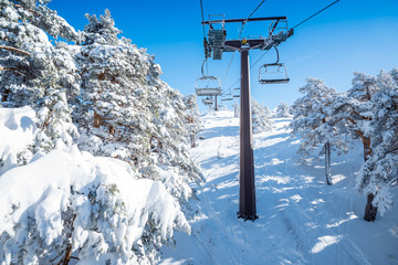 A winter view of a ski resort full of fresh snow taken from the chairlift going through a forest, in Madrid, Spain