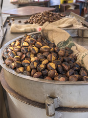 Roasted chestnuts cooked on a bin with wood fire. Near jute bags for raw chestnuts. Outdoor sales stall.
