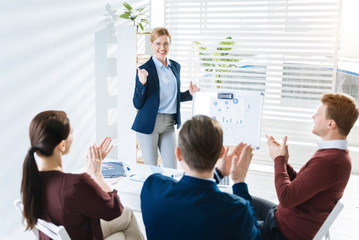  Great performance. Budding inspired  female colleague standing  near white board while showing thumbs and grinning