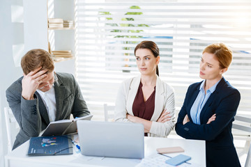 Big failure. Serious focused three colleagues thinking over problem while women staring at the man and crossing hands 