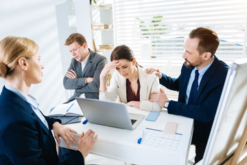 Crying at work. Stressful upset female colleague crying while her colleagues calming her down and  sitting