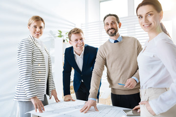 Ideal blueprint. Ambitious happy four  colleagues staying while laughing and gazing at the camera