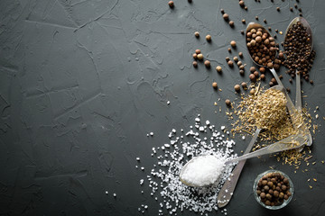  pepper black peas and salt and green dried grass seasoning in metal antique spoons and hot chili peppers on a dark concrete  beton background
