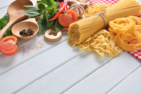 Pasta spaghetti, farfalle, linguine with vegetables and spices on white wooden table