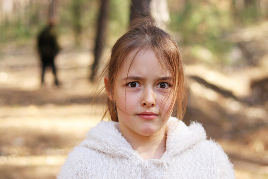 Frightened little girl alone in the forest with dark silhouette at background, children safety concept