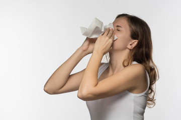 A beautiful brunette woman becomes ill with a cold and runny nose, sneezes and coughs into a white paper kerchief