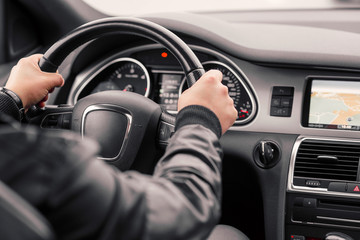 Businessman driving luxury modern car in the city. Close up man's hand on the wheel of the car.