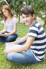 Fototapeta premium Couple of teenagers happy outdoor making school tests seated on the grass