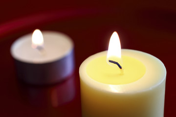 .Close up of a burning wax candle against a red background.