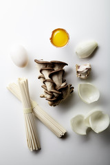 Asian cuisine ingredients on white background. Udon noodles, egg yolk, onion, garlic and oyster mushrooms
