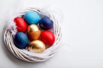 Eggs painted in various colors arranged with feathers in twig wreath on white background. Easter traditions concept.