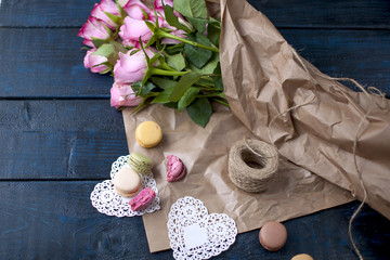 A bouquet of roses is pink, in gray paper and white hearts. Sweet pasta macaroons of different colors, on Valentine's Day. A free place for text or advertising.