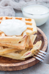 Homemade savory belgian waffles with bacon and shredded cheese, served with plain yogurt on wooden plate, vertical