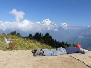 Hiker relaxing on Poon Hill, Dhaulagiri range on the backround - one of the most visited Himalayan view points in Nepal, view to snow capped Himalaya