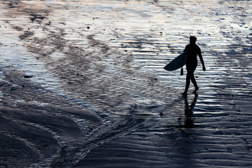 A surfer leaves the beach after enjoying a evening surf nearby Cabaret sur mer in Brittany, France  