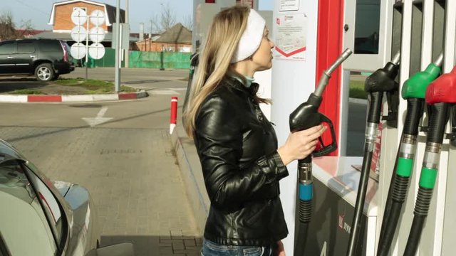 Woman driver at the gas station. The man pours expensive gasoline into the car.