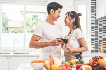 Obraz na płótnie Canvas Asian lovers or couples drinking wine in kitchen room at home. Love and happiness concept Sweet honeymoon and Valentine day theme