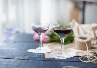 Two glasses of red wine. A bouquet of pink roses in brown paper. Color pastry macaroni. Near the window. Free space for text or postcards.