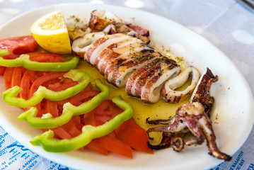 Seafood, grilled calamari served with tomatoes, green peppers and lemon in traditional Greek tavern. Naxos island. Greece.