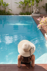 back view of young woman in swimsuit and hat sitting in pool of hotel - obrazy, fototapety, plakaty