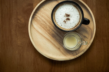 hot cappuccino coffee with cinnamon powder in black cup on wood table