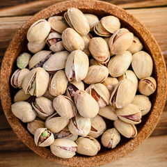 a bunch of pistachios nuts in a brown cork plate on a wooden background.
