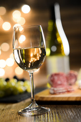 glass of white wine with french cheese and delicatessen in restaurant wooden table with romantic dim light and cosy atmosphere
