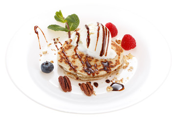 Serving pancakes with ice cream on the plate. Decorated with chocolate syrup, nuts and fresh berries and mint. Isolated on white background.