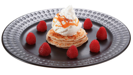 Serving pancakes with ice cream, whipped cream and raspberries on black plate. Decorated with caramel syrup. Isolated on white background.