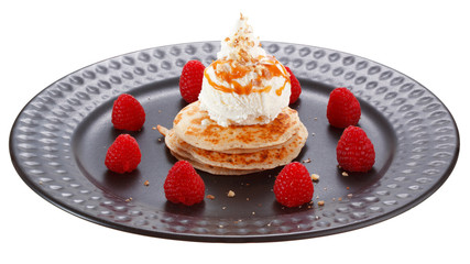 Serving pancakes with ice cream, whipped cream and raspberries on black plate. Decorated with caramel syrup and nuts. Isolated on white background.