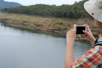traveler man with backpack travel at forest & lake. tourist backpacker use smart phone to take photo. lifestyle, summer vacation concept