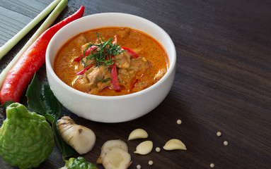 Chicken Panang curry in the white bowl and fresh spice on brown wooden background Thai food