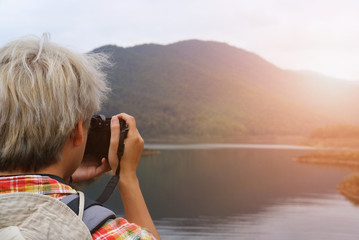 traveler man with backpack travel at mountain & lake. tourist backpacker use camera to take photo. lifestyle, summer vacation concept