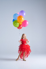 Obraz na płótnie Canvas Joyful charming girl in red dress holding colorful balloons