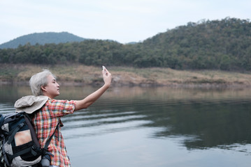 traveler hiker man with backpack hiking near lake. tourist backpacker use smart phone to take selfie photo. travel lifestyle, summer vacation concept