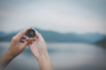 hand holding compass for searching direction outdoor. man seeking way with nature background. travel lifestyle, summer vacation concept