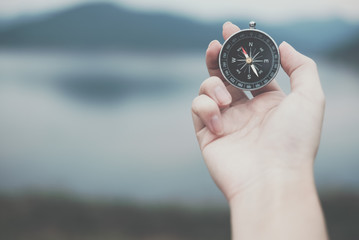 hand holding compass for searching direction outdoor. man seeking way with nature background. travel lifestyle, summer vacation concept - obrazy, fototapety, plakaty