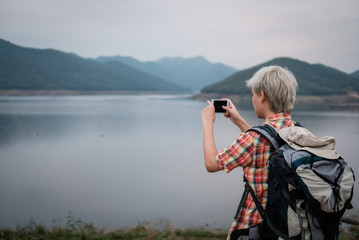 Obraz premium traveler hiker man with backpack hiking near lake. tourist backpacker use smart phone to take photo in the evening. travel lifestyle, summer vacation concept