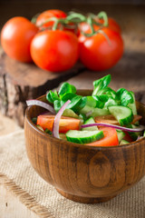 Salad with greens, tomatoes, red onions and cucumber on wood plate with wood background, overhead view with fork