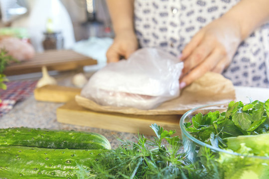 Fresh greens, dill, parsley, lettuce, and cucumbers on the kitchen table. Woman unpacking groceries out of focus. Shallow depth of field. Copy space